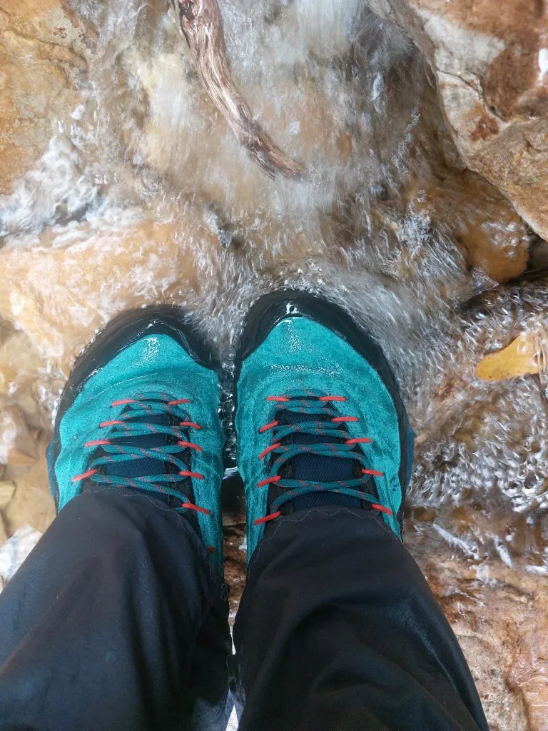 Image of blue hiking boots almost submerged in some water in a river bed.